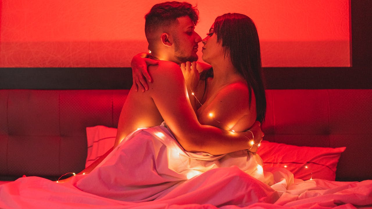 Couple embracing under fairy lights on a bed with a red ambiance